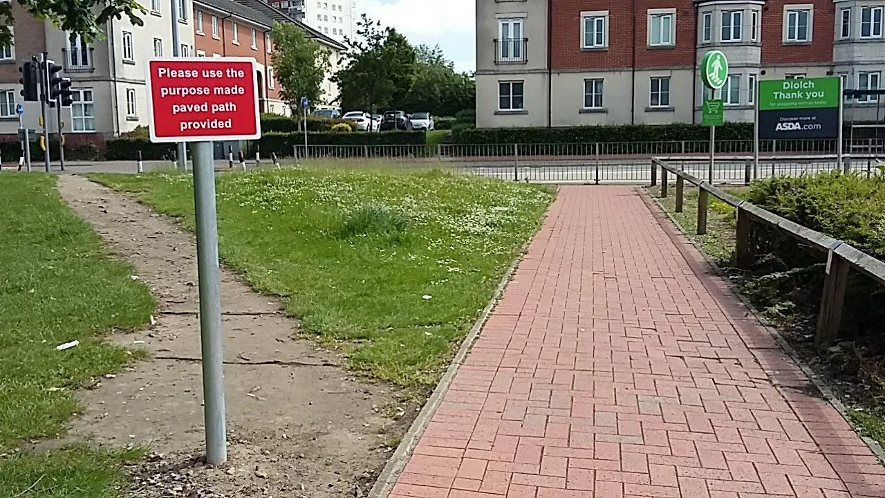 A paved brick path beside a worn dirt trail cut through the grass